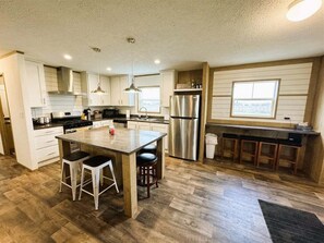 A kitchen with a central island, stainless steel appliances, and a bar area.