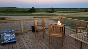A wooden deck with chairs and a table, overlooking a field.