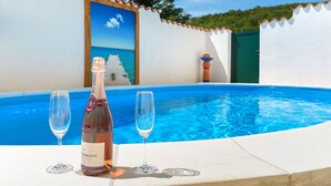 A poolside setting with a bottle of Brut Dargent champagne and two glasses. - A rustic stone house with pool and sea views. (Ripenda Kosi)