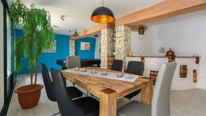 A modern dining area with a wooden table, black and gray chairs, a potted plant, and stone pillars. - A rustic stone house with pool and sea views. (Ripenda Kosi)