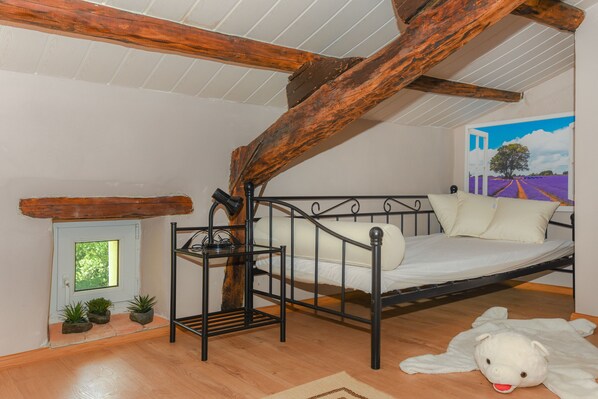 A bedroom with a metal bed frame, a wooden ceiling beam, a small window, and a painting of a landscape. - A rustic stone house with pool and sea views. (Ripenda Kosi)