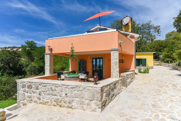 Ein modernes Haus mit Steinfundament, einem Balkon mit rotem Sonnenschirm und einer kleinen Sitzgelegenheit im Freien.