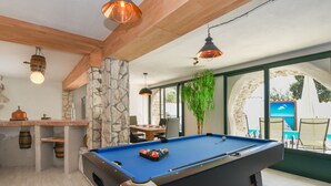 A pool table with a blue felt surface, surrounded by stone pillars and wooden beams. - A rustic stone house with pool and sea views. (Ripenda Kosi)