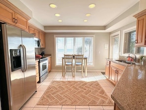 A modern kitchen with a refrigerator, oven, microwave, dining table with chairs, and a window with blinds. - Luxury Ocean View Villa w/ Pool on Hilton Head (Hilton Head Island)