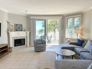 A living room with a fireplace, a sofa, a coffee table, and a view of the outside.
