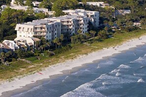 A coastal residential area with beachfront properties, including multi-story buildings with balconies, a sandy beach, and ocean waves.