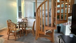 Un espace repas avec un escalier en bois, une cuisine à l’arrière-plan et une vue sur l’extérieur.