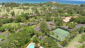 Vue aérienne d’un complexe hôtelier doté d’un court de tennis, d’une piscine et offrant une vue sur l’océan.