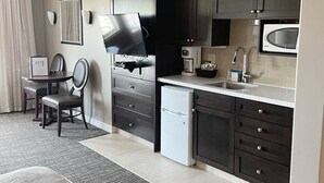 Een moderne keuken met donkere kastjes, een ingebouwde magnetron en een koffiezetapparaat. Er is een eethoek met een tafel en stoelen.