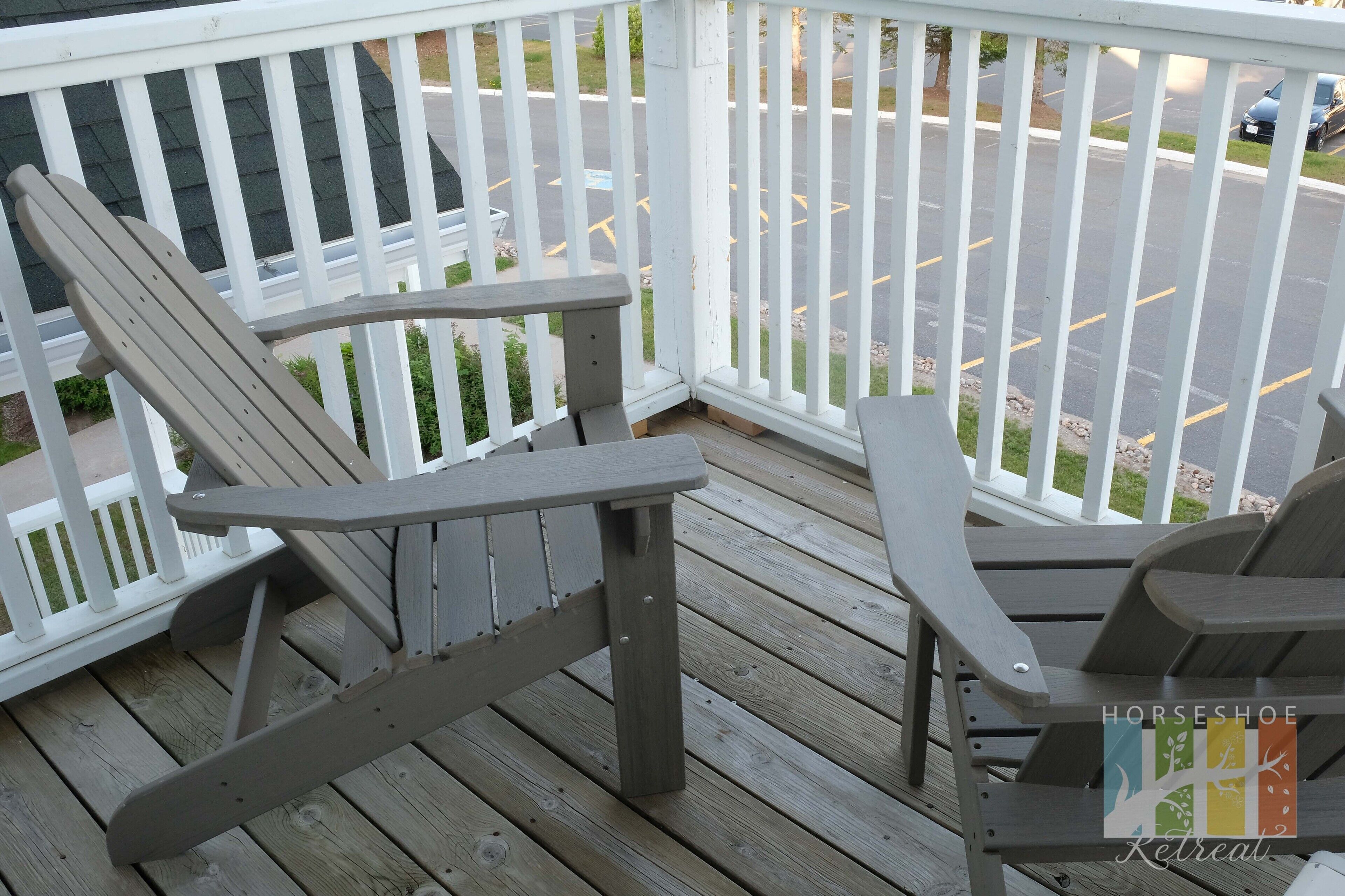 A wooden deck with two Adirondack chairs and a small table.