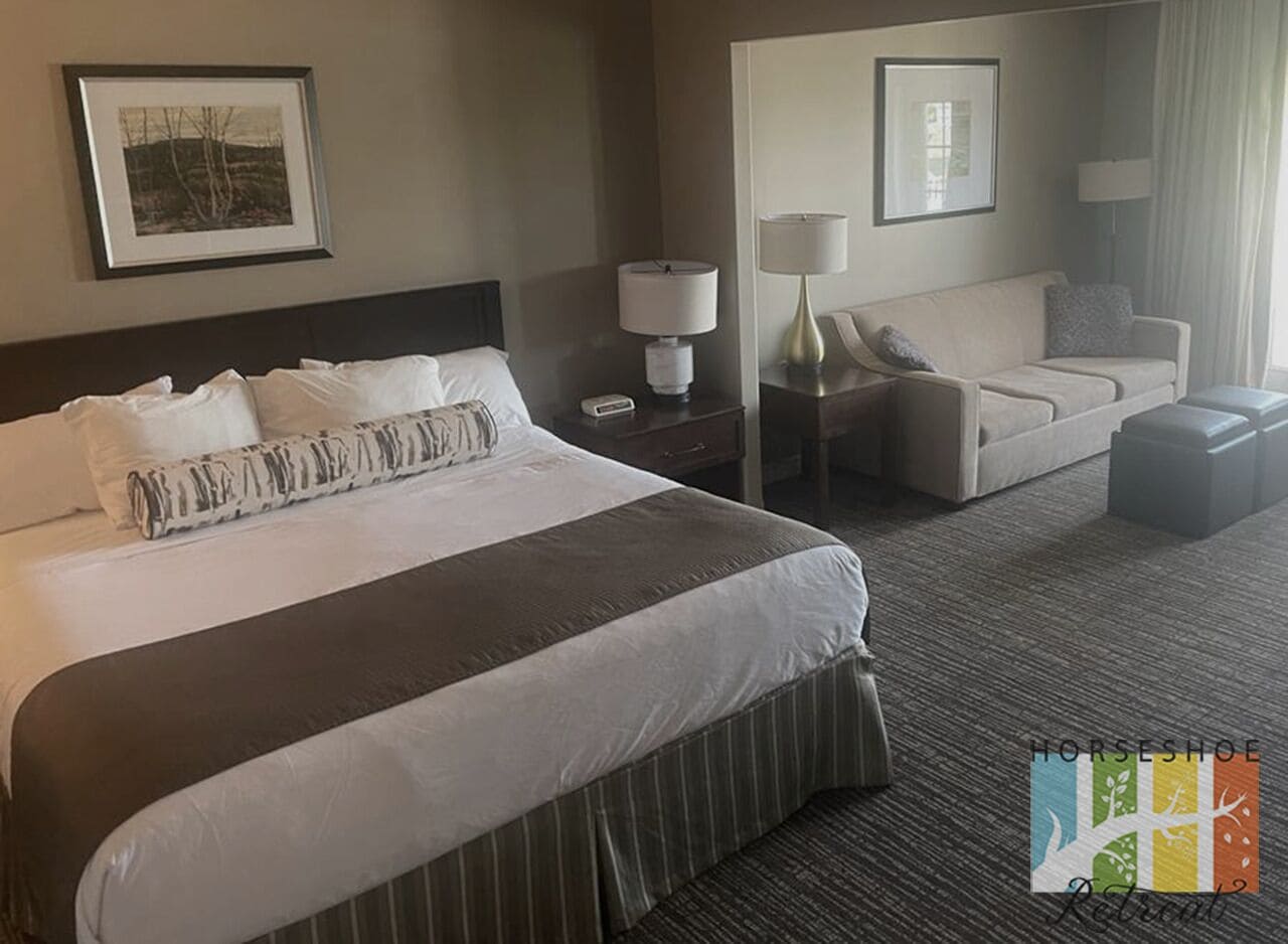 A hotel room with a large bed, a sofa, a nightstand with a lamp, and a framed picture on the wall.