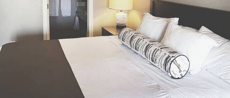 A hotel room with a large bed, a nightstand with a lamp, a framed picture on the wall, and a door leading to a bathroom.