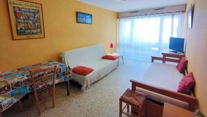 Una habitación con sofá, una mesita, televisión y ventana con cortinas.