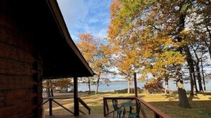 A wooden deck with a table and chairs, overlooking a lake and autumn trees.