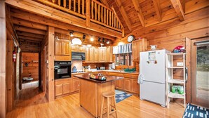 A wooden cabin kitchen with a central island, wooden cabinets, a refrigerator, and a microwave.
