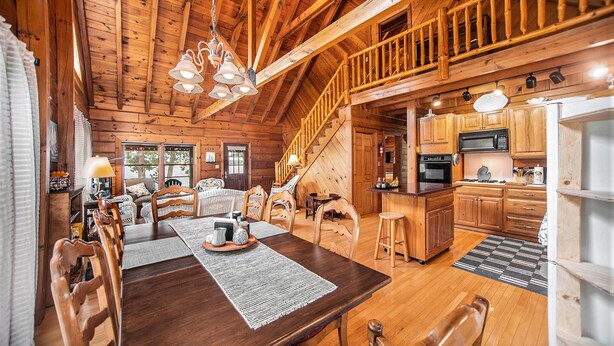 A spacious wooden cabin with a dining area, kitchen, and a staircase leading to a loft.
