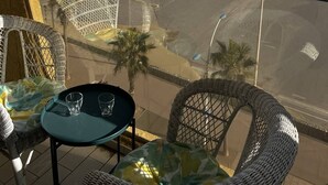 Uma varanda com cadeiras de vime e uma mesa, com vista para uma praia e para o oceano.