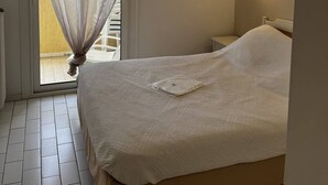 Quarto com cama, janela com cortinas leves e luminária na parede, com vista para o exterior.