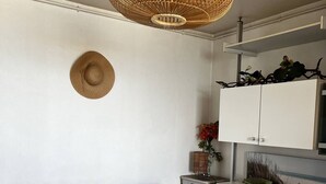 Quarto com um sofá azul, uma luminária pendente de vime, um armário branco e uma mesinha de cabeceira com uma planta.