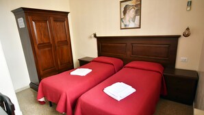 A hotel room with two single beds, wooden headboards, a wardrobe, and a painting on the wall. - Via Curtatone 12 Apartment (Rome)