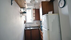 A compact kitchen with wooden cabinets, a white refrigerator, and a clock on the wall. - Via Curtatone 12 Apartment (Rome)