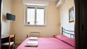 A bedroom with a bed, a desk, a chair, a window, and an air conditioner. - Via Curtatone 12 Apartment (Rome)