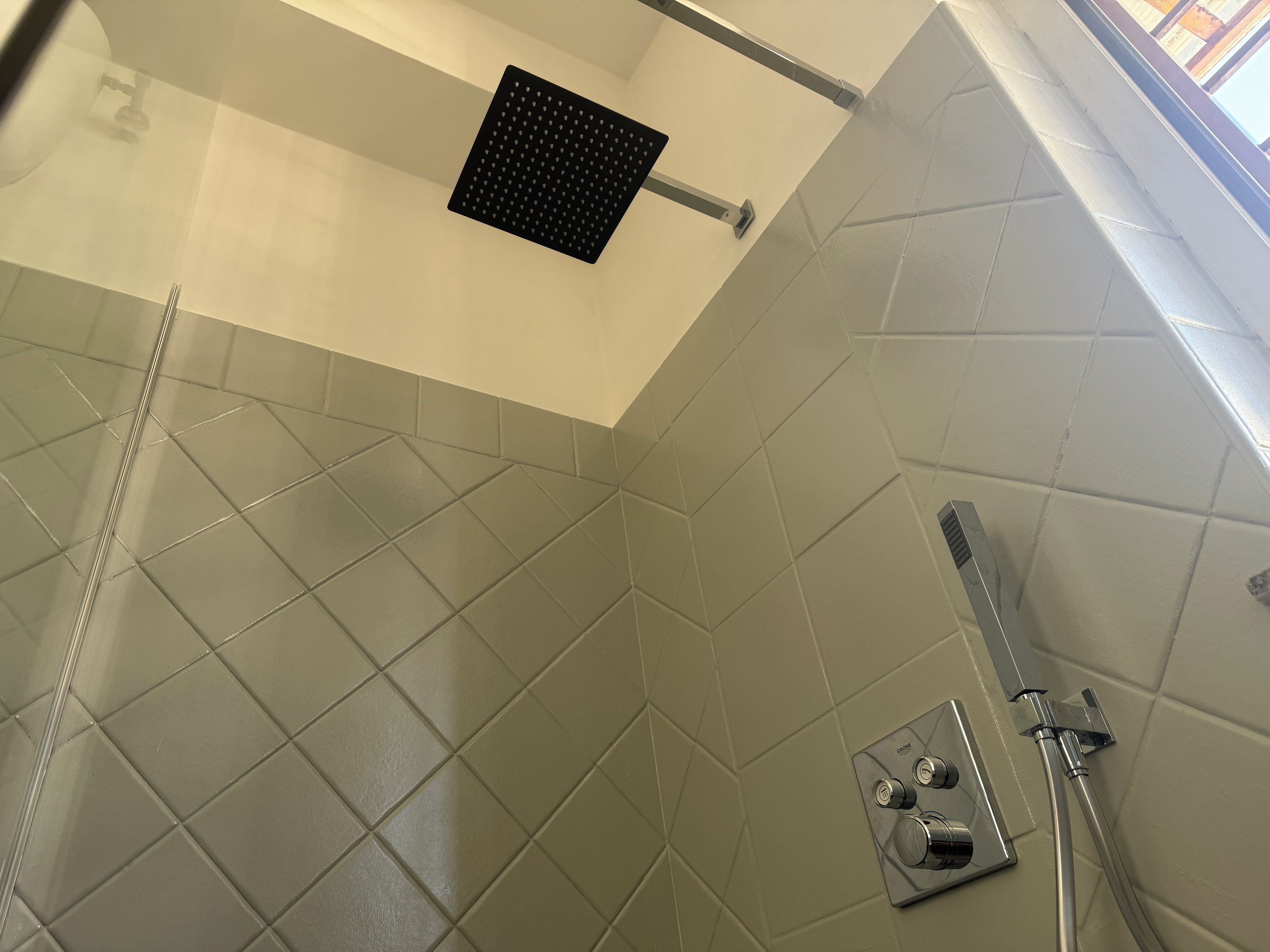 Un espace douche avec un mur carrelé, une douchette à main et un panneau de commande.