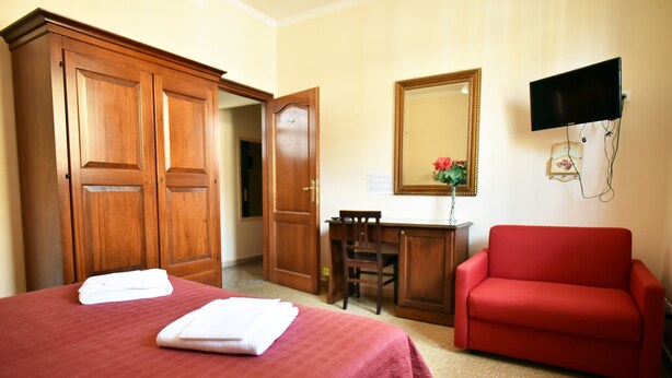 A hotel room with a bed, a red sofa, a desk, a chair, a wooden wardrobe, and a flat-screen TV mounted on the wall. - Via Curtatone 12 Apartment (Rome)