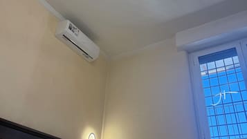 Habitación de hotel con cama, aire acondicionado de pared, ventana con vistas y lámpara de techo.