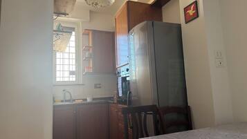 Cocina compacta con muebles de madera, un refrigerador y una mesa de comedor con mantel estampado.