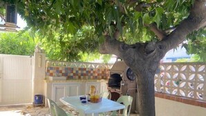 En udendørs terrasse med et bord, stole, grill og flisebeklædt bagpanel.