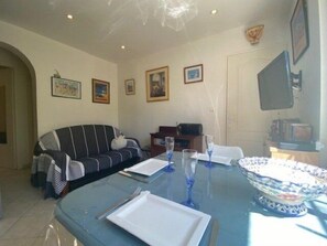 A dining area with a table set for two, a sofa, and framed artwork on the walls.