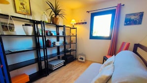 A room with a bed, a bookshelf, a window with curtains, and a small table with a plant.