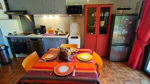A compact kitchen with modern appliances, a dining table set for four, and a red cabinet.