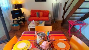 A dining area with a table set for two, a sofa, a TV, and a staircase.