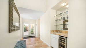 A hallway with a bench, a glass display case, and a kitchen area with a dishwasher.