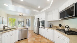 A modern kitchen with white cabinetry, stainless steel appliances, and a large black microwave.