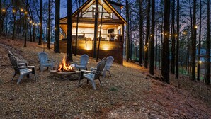 Eine Holzhütte mit Feuerstelle und Sitzgelegenheiten in Waldumgebung.