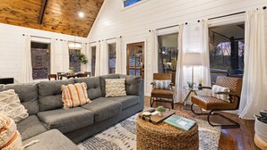 Ein gemütliches Wohnzimmer mit grauem Sofa, Weidenhocker und einem Essbereich mit Tisch und Stühlen.