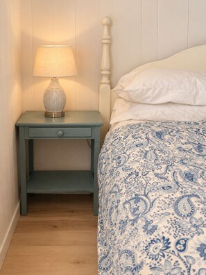 A bedroom with a bed, a nightstand with a lamp, and a wooden floor. - Little Haven Cottage - Ocean view 2 bedroom cottage with beach access. (Mount Stewart)