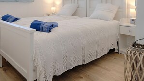 A white bed with a knitted blanket, two bedside lamps, and a blue towel on the bed. - Charming apartment ideally located - Swimming pool - Air conditioning (Mimizan)