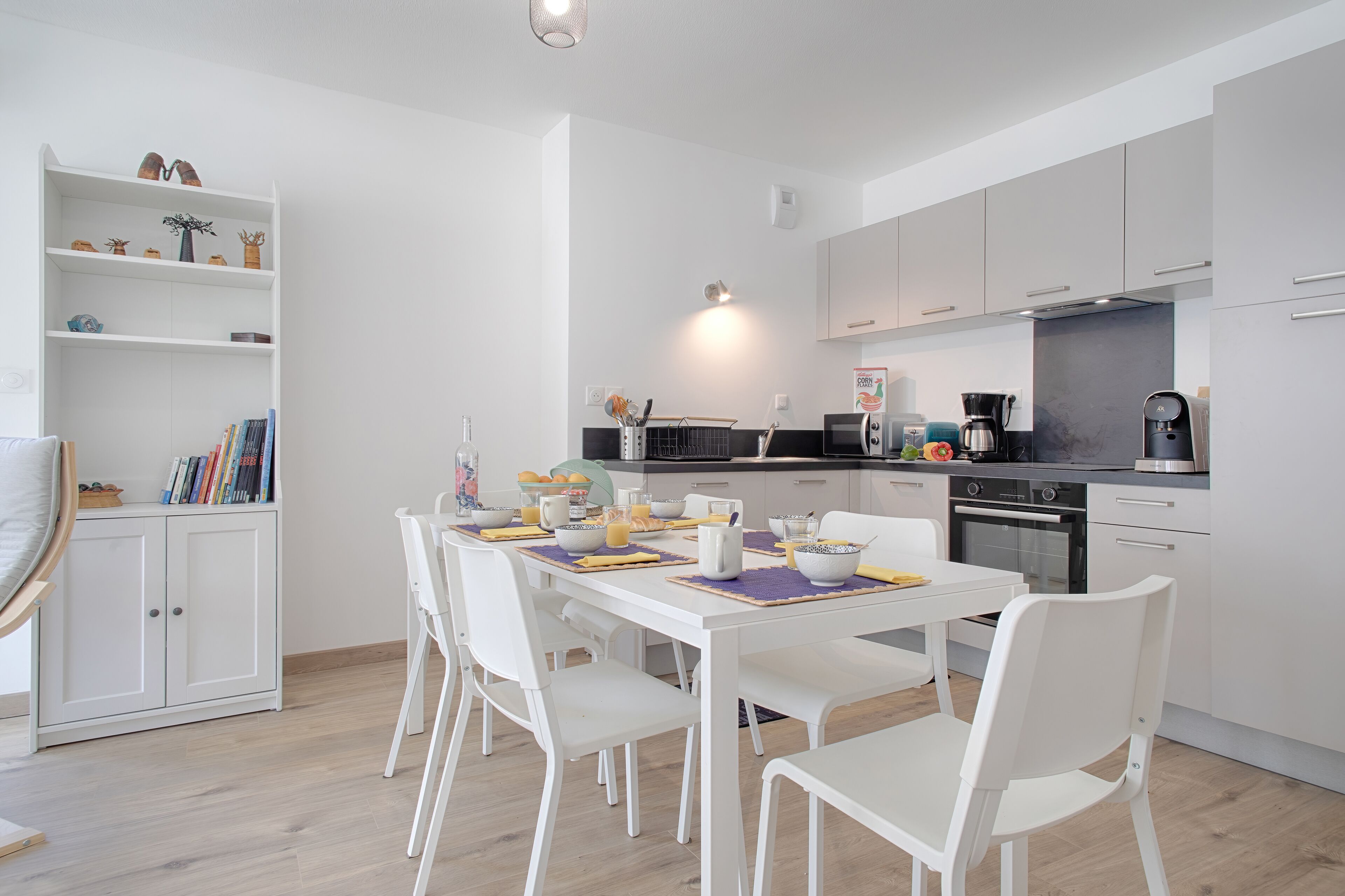 A modern kitchen with white cabinetry, a dining table set with chairs, and a coffee machine.
