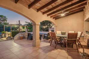 An outdoor patio area with a tiled floor, wooden chairs, a table, and a ceiling fan.
