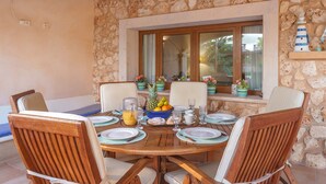 A round wooden dining table with chairs, a fruit bowl, and various dining items. - Villa "Sa Caseta Rustic Villa" with Pool, Terraces & Wi-Fi (Tourist Tax Included) (Cala D'or)