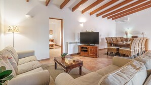 A living room with a sofa, coffee table, TV, dining table with chairs, and a wooden ceiling. - Villa "Sa Caseta Rustic Villa" with Pool, Terraces & Wi-Fi (Tourist Tax Included) (Cala D'or)
