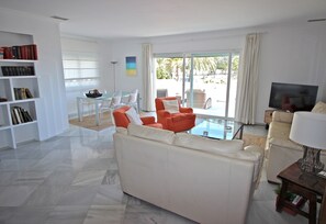 Uma sala de estar moderna com um sofá, poltronas, uma televisão e uma estante.