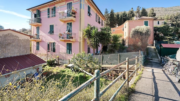 Un edificio rosa con balcones, un jardín cercado y bicicletas.