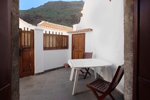 A courtyard with a white table and wooden chairs, a wooden door, and a window with a lattice design.
