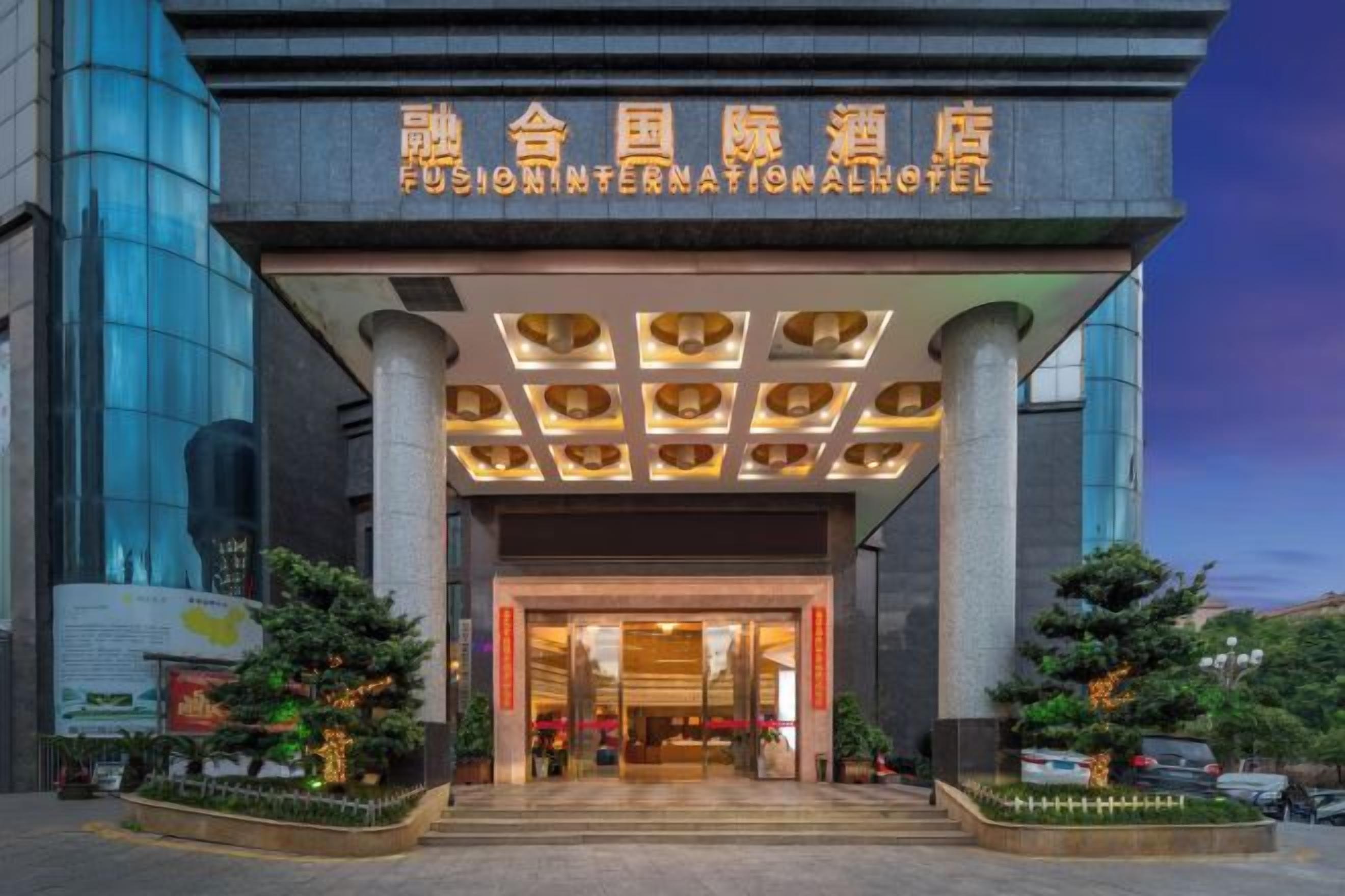Entrada de hotel con diseño moderno, que presenta un gran letrero con caracteres chinos, un área de recepción cubierta y un espacio exterior bien cuidado con plantas.