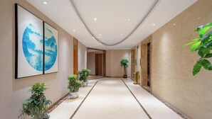 A corridor with a marble floor, potted plants, and framed artwork on the walls. - Fusion International Hotel (Yizhang)